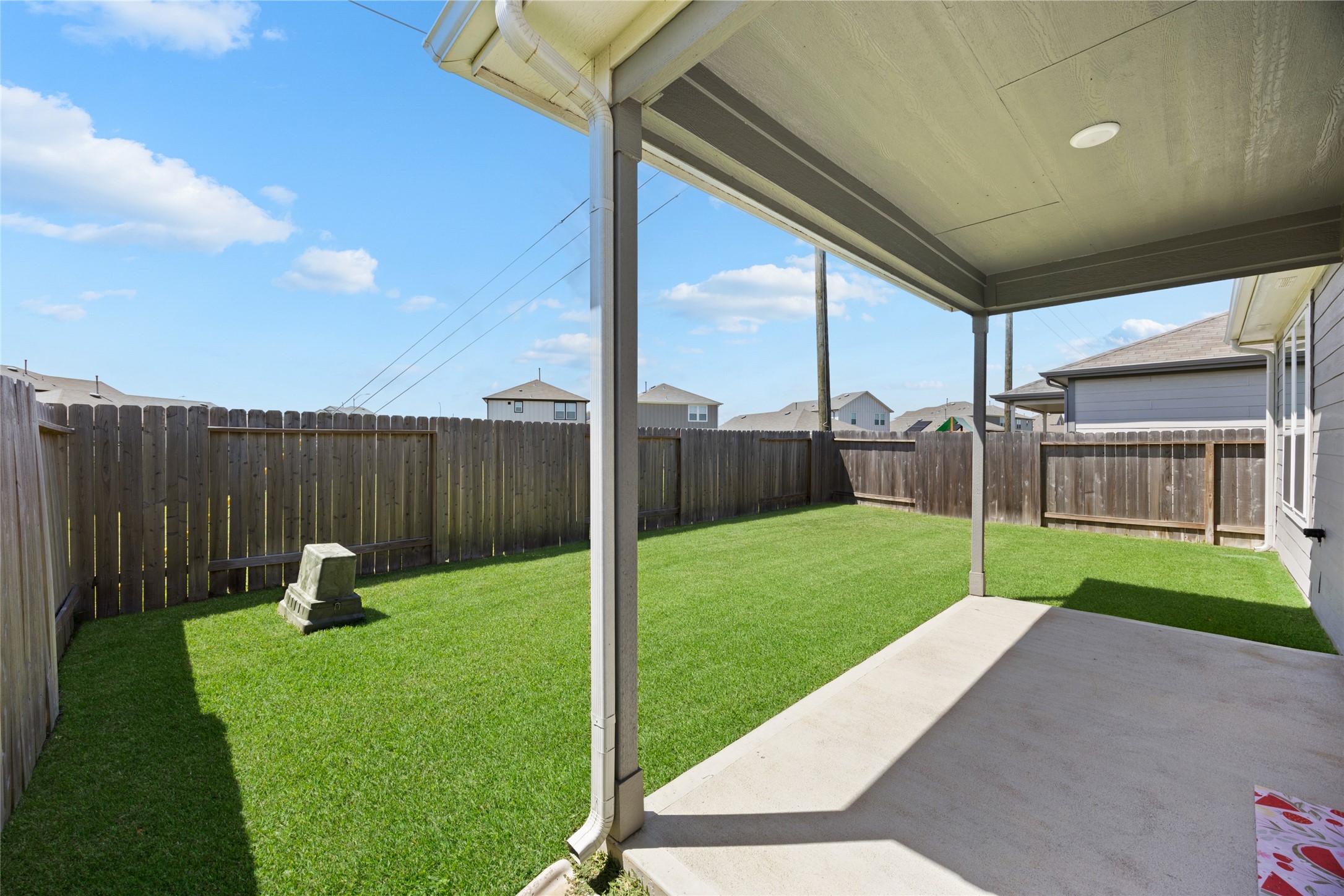 17907 Grain Auger Road Hockley, TX 77447 - Photo 3 of 24 backyard with a well-maintained lawn, surrounded by a wooden privacy fence. There's a covered patio providing shade, making it ideal for outdoor relaxation.