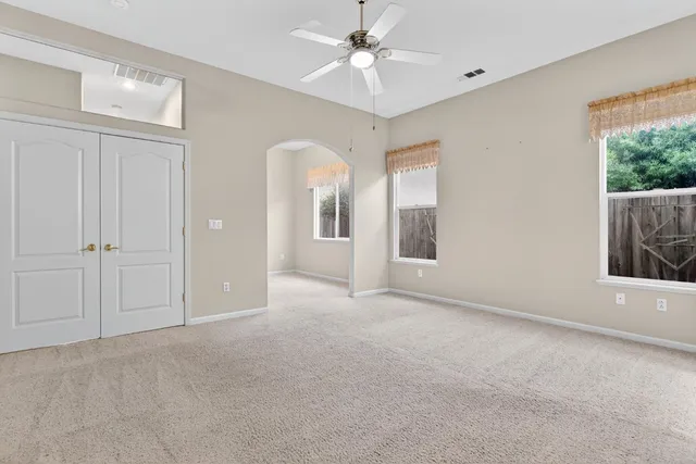 an empty room with chandelier fan and windows