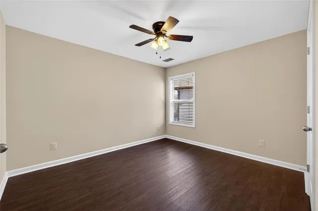 a view of an empty room with wooden floor and a ceiling fan