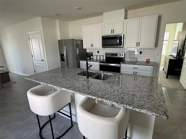 a kitchen with stainless steel appliances granite countertop a refrigerator a stove a sink a dining table and chairs
