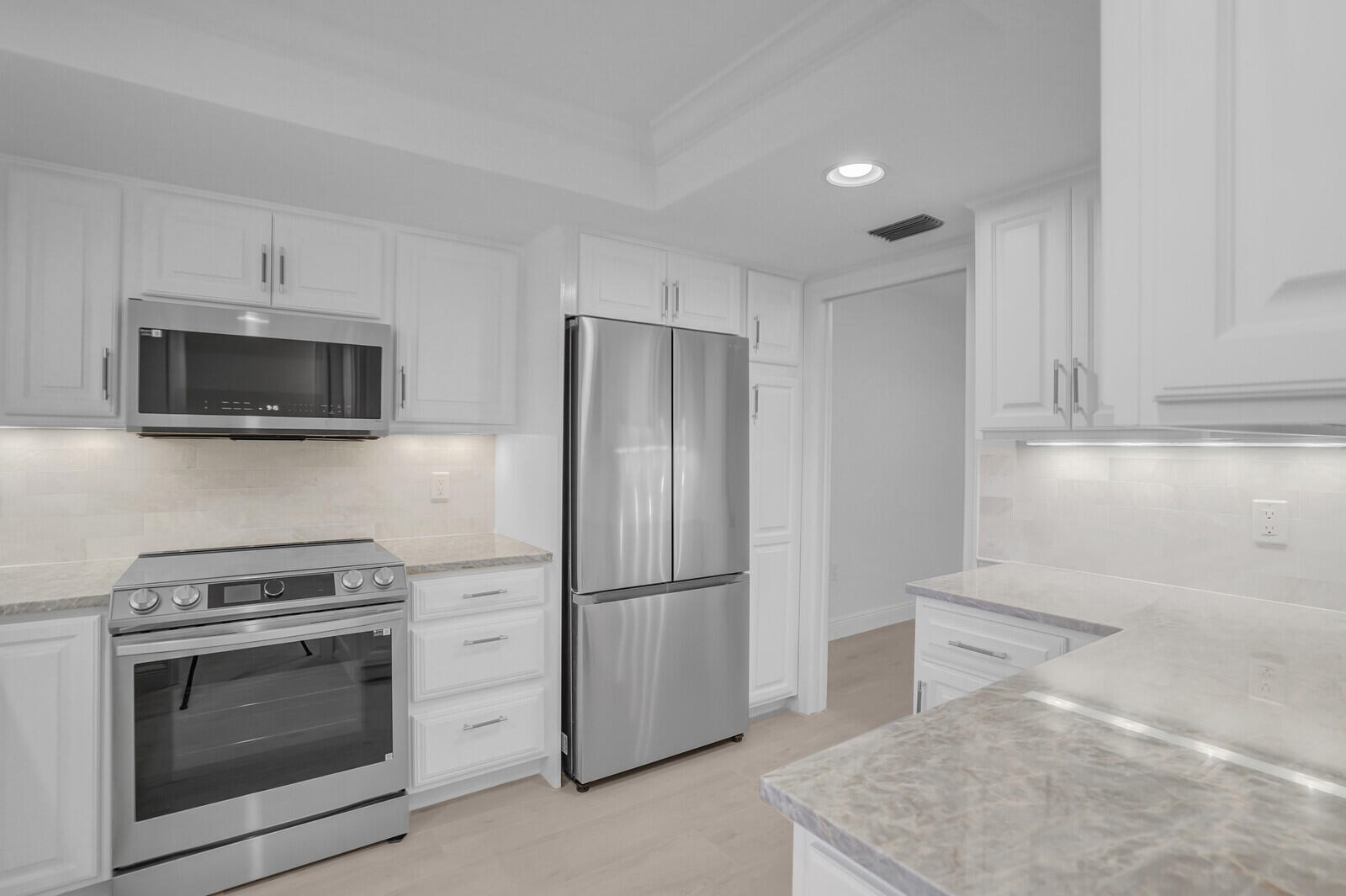 145 Atlantis Boulevard, Unit 104 Atlantis, FL 33462 - Photo 21 of 49 a kitchen with stainless steel appliances white cabinets and a refrigerator