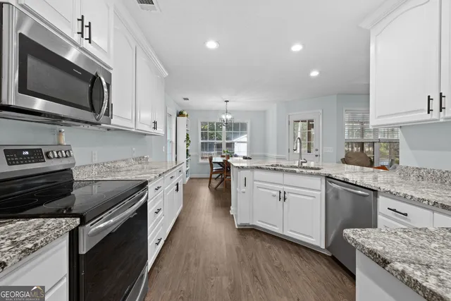 a large kitchen with stainless steel appliances granite countertop a stove top oven a sink dishwasher a microwave oven and a dining table with wooden floor