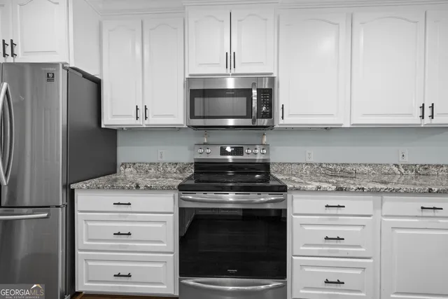 a kitchen with granite countertop white cabinets and stainless steel appliances