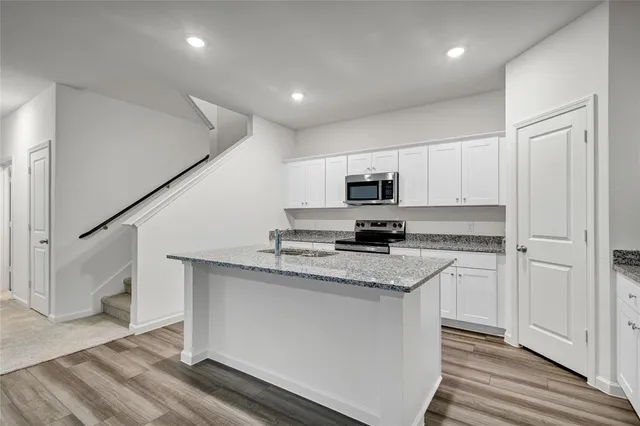 a kitchen with stainless steel appliances granite countertop a sink a stove a microwave a refrigerator and white cabinets