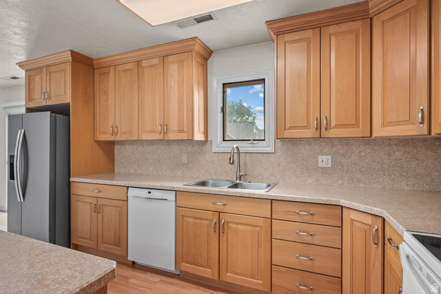 328 Heather Ridge Circle Sandy, UT 84070 - Photo 3 of 28 Kitchen featuring natural wood cabinetry, light-toned countertops, double basin stainless steel sink, and wood-finish flooring