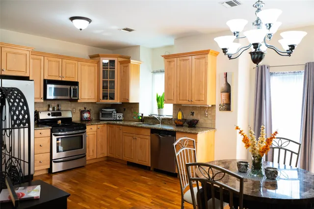 a kitchen with stainless steel appliances granite countertop a stove top oven a sink dishwasher a dining table and chairs with wooden floor