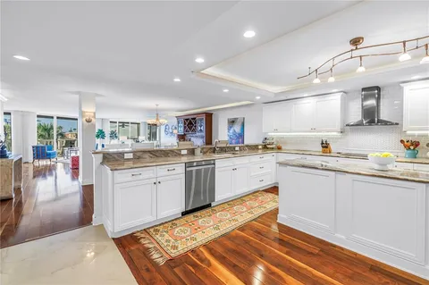 a kitchen with stainless steel appliances granite countertop a refrigerator a sink dishwasher and white cabinets with wooden floor