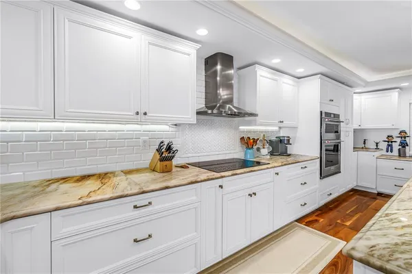 a kitchen with stainless steel appliances granite countertop a refrigerator a sink dishwasher and white cabinets with wooden floor