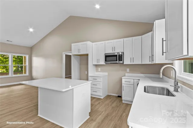 a kitchen with stainless steel appliances a stove top oven a sink a refrigerator white cabinets and wooden floor