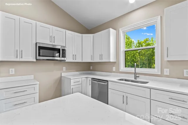 a kitchen with white cabinets appliances a sink and a window