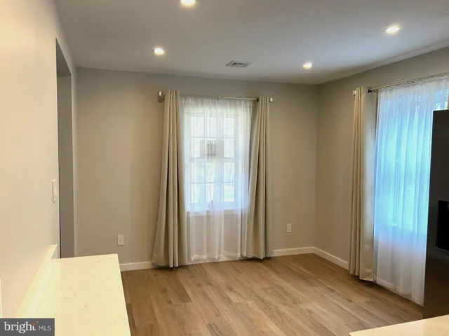 an empty room with wooden floor and windows with curtains