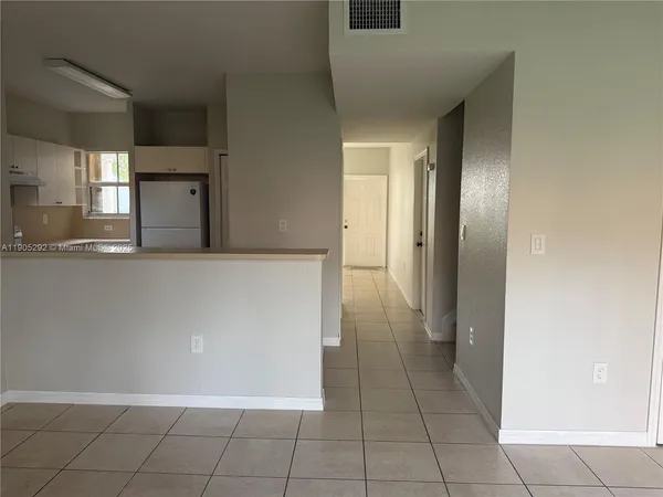 a view of a refrigerator in kitchen and an empty room