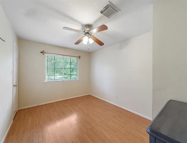 an empty room with wooden floor ceiling fan and windows