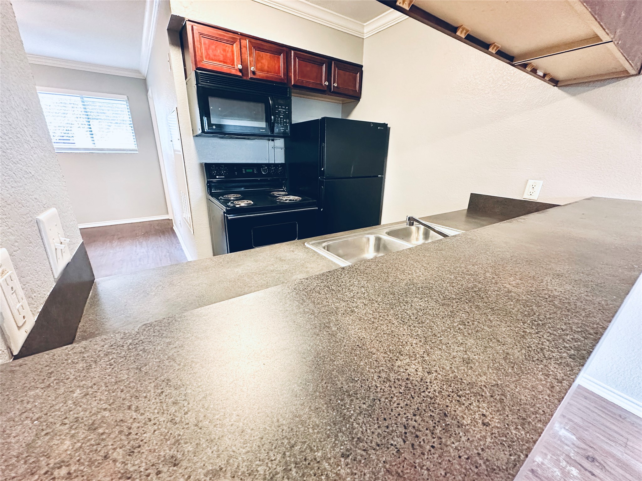 805 South Center Street, Unit 108 Austin, TX 78704 - Photo 4 of 14 Kitchen featuring a textured wall, black appliances, crown molding, wood finished floors, and light countertops