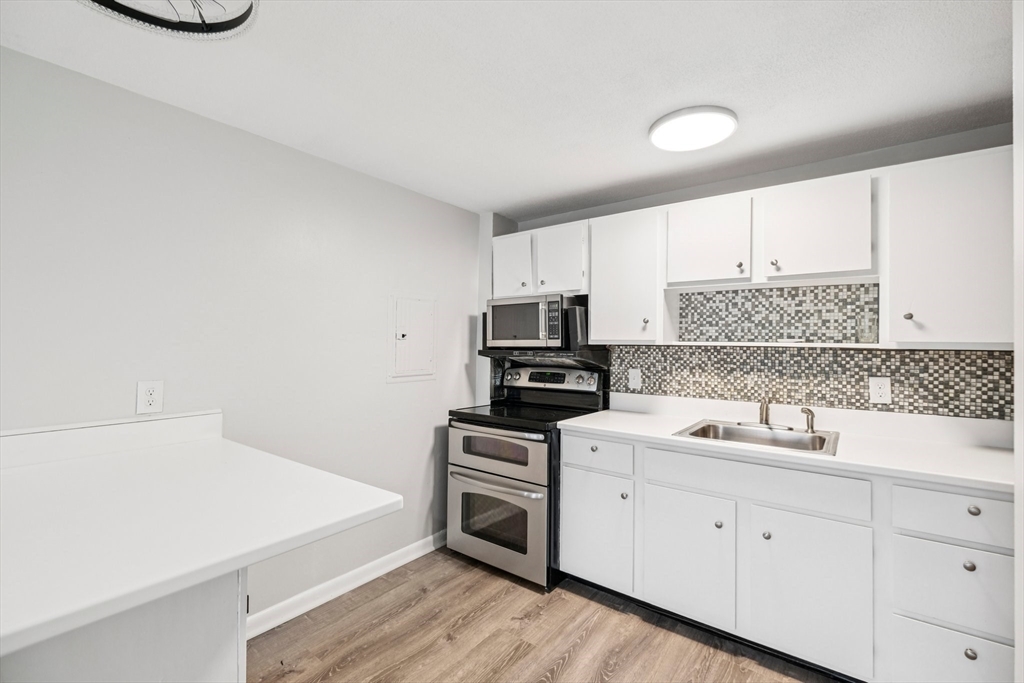 770 Cummins Highway, Unit 22 Boston, MA 02126 - Photo 14 of 28 a kitchen with a sink dishwasher a stove and white cabinets with wooden floor