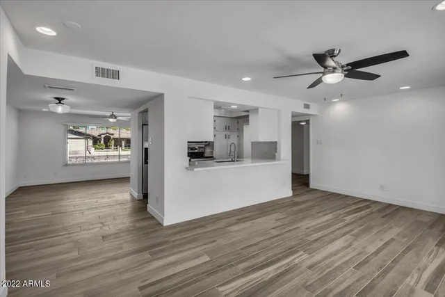 a view of an empty room with kitchen and window
