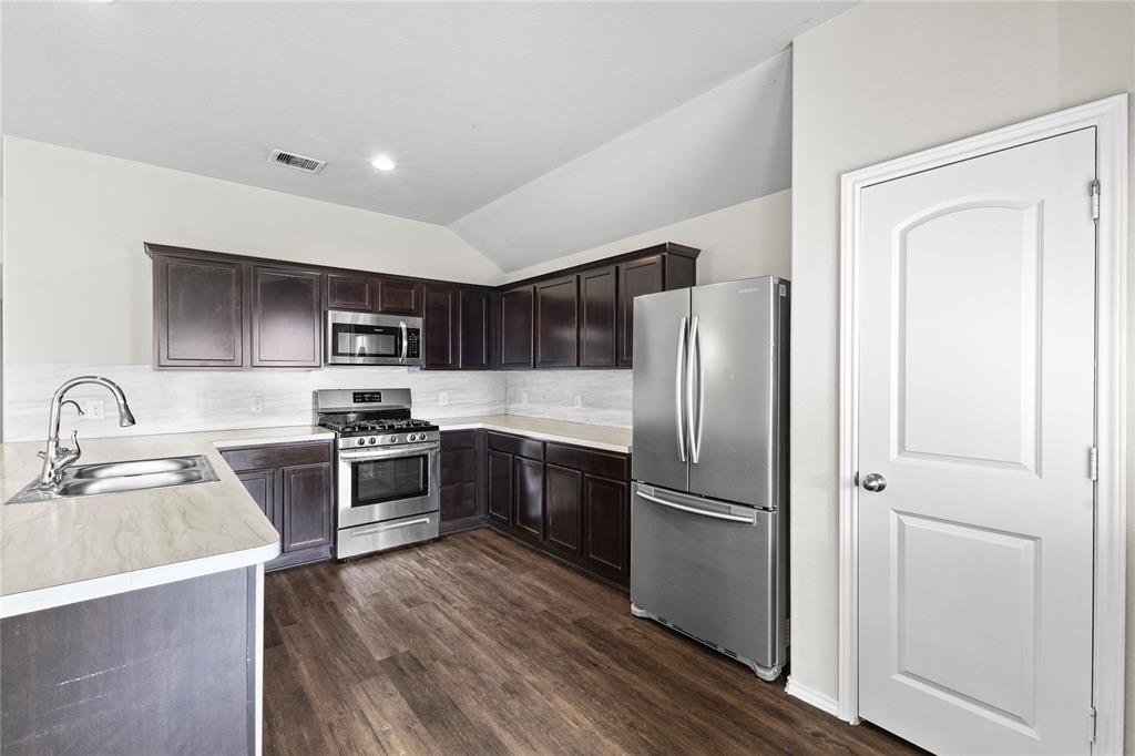 15454 Arce Rojo Street Channelview, TX 77530 - Photo 12 of 32 Kitchen with light countertops, appliances with stainless steel finishes, dark brown cabinetry, tasteful backsplash, and lofted ceiling