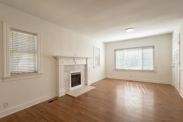 an empty room with wooden floor fireplace and windows