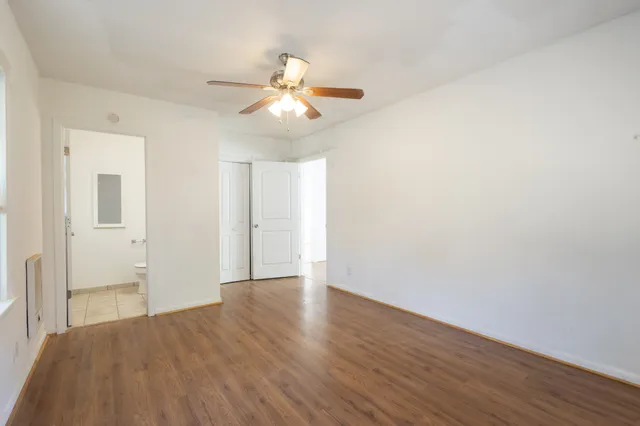 an empty room with wooden floor fan and windows