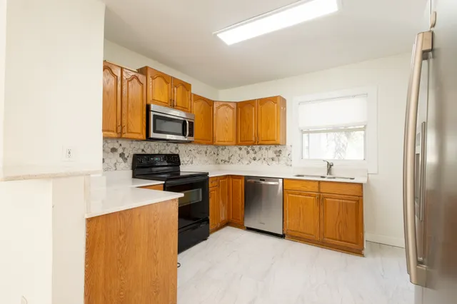 a kitchen with stainless steel appliances granite countertop a stove top oven a sink dishwasher and a refrigerator with wooden cabinets