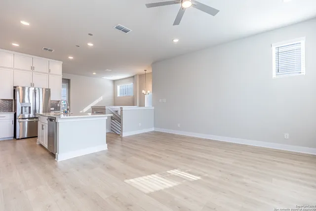 a view of an empty room with kitchen and window