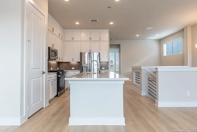 a kitchen with stainless steel appliances a stove top oven a sink a refrigerator and white cabinets