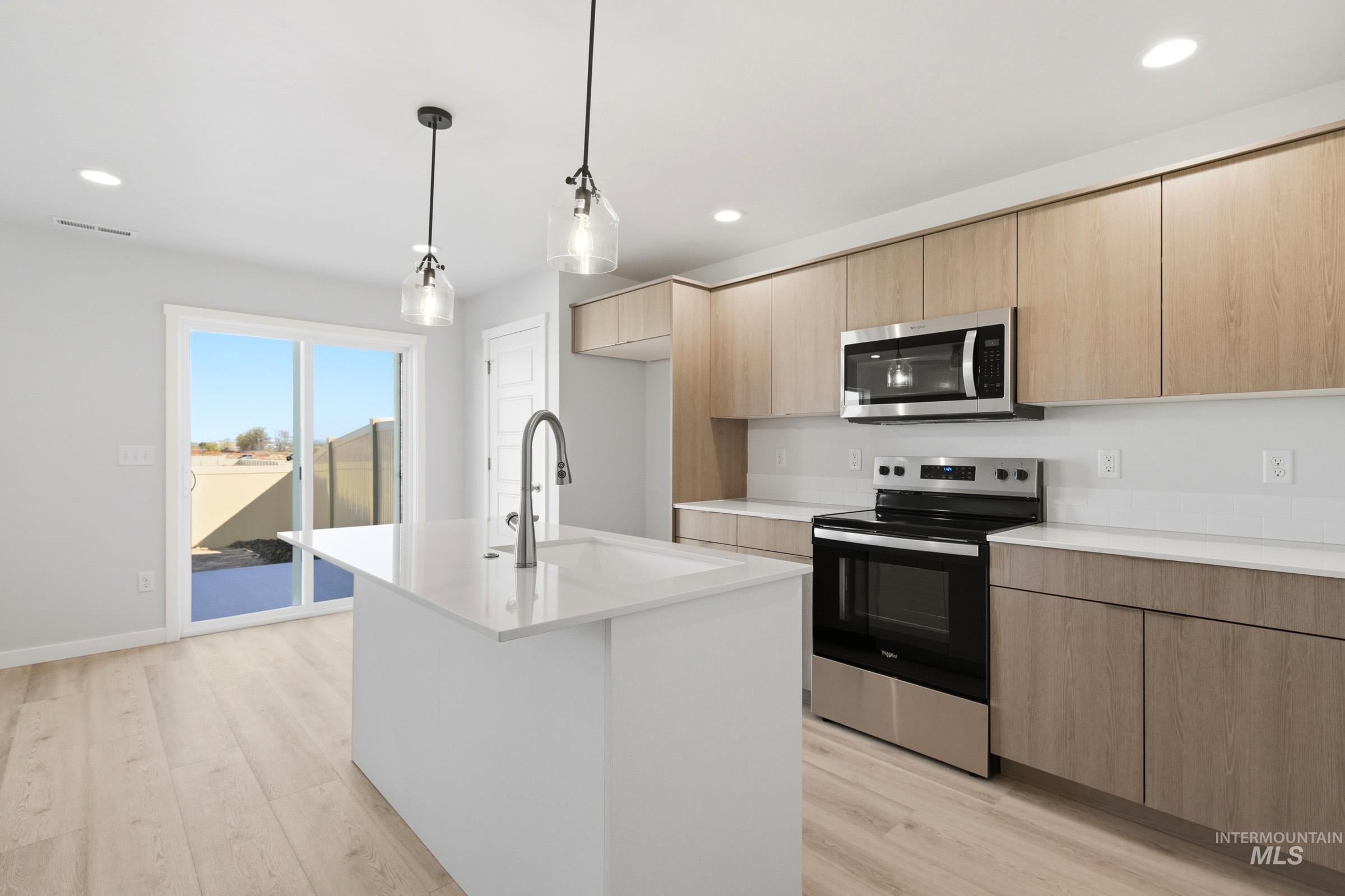 10800 Rutland Street Caldwell, ID 83605 - Photo 6 of 21 Modern kitchen featuring a central island with a sink, light wood-finish cabinetry, stainless steel appliances, and wood-finish flooring
