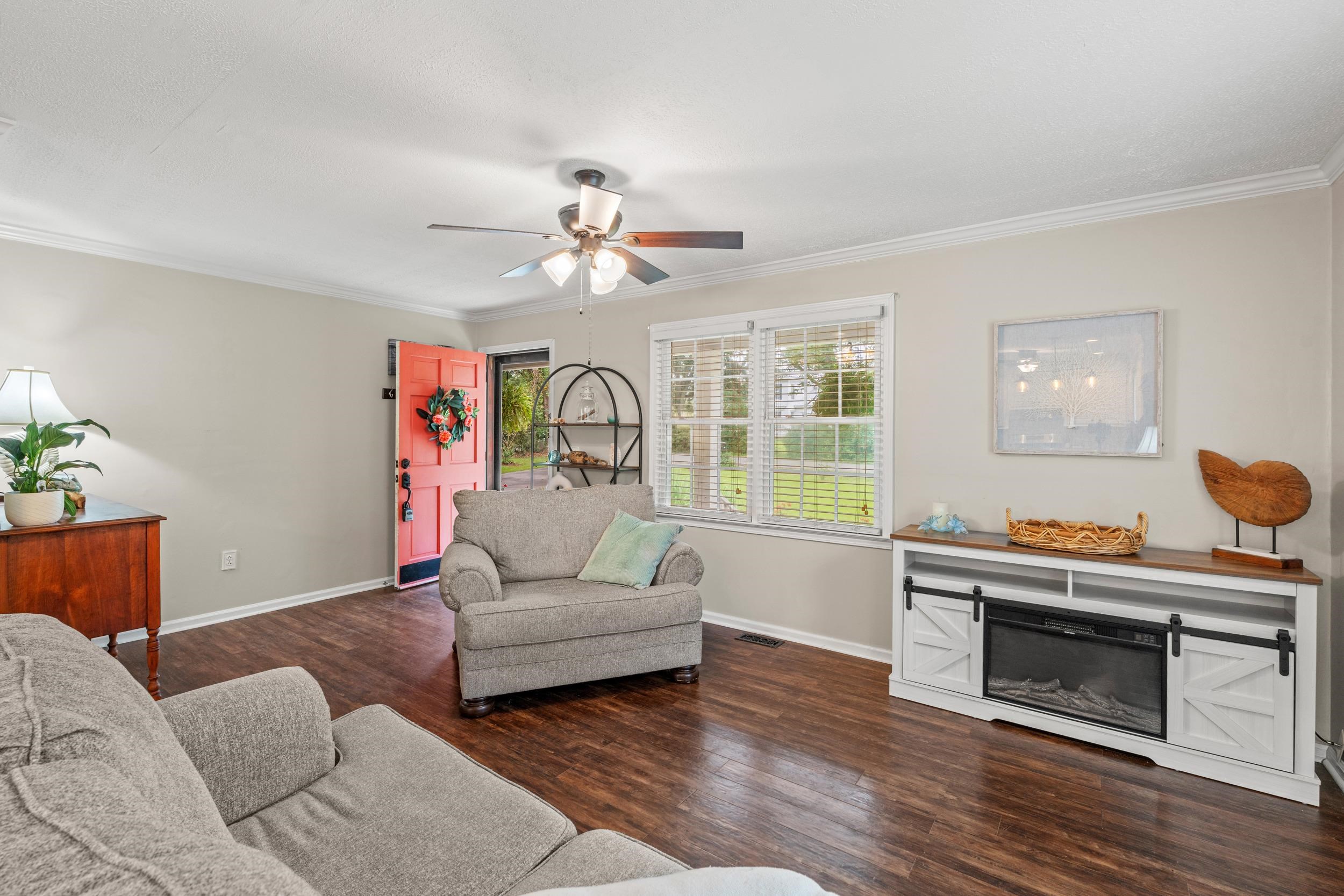 208 Bethea Street Latta, SC 29565 - Photo 6 of 36 Living room with dark wood-style floors, ornamental molding, ceiling fan, and a glass covered fireplace