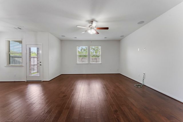 an empty room with wooden floor chandelier fan and windows