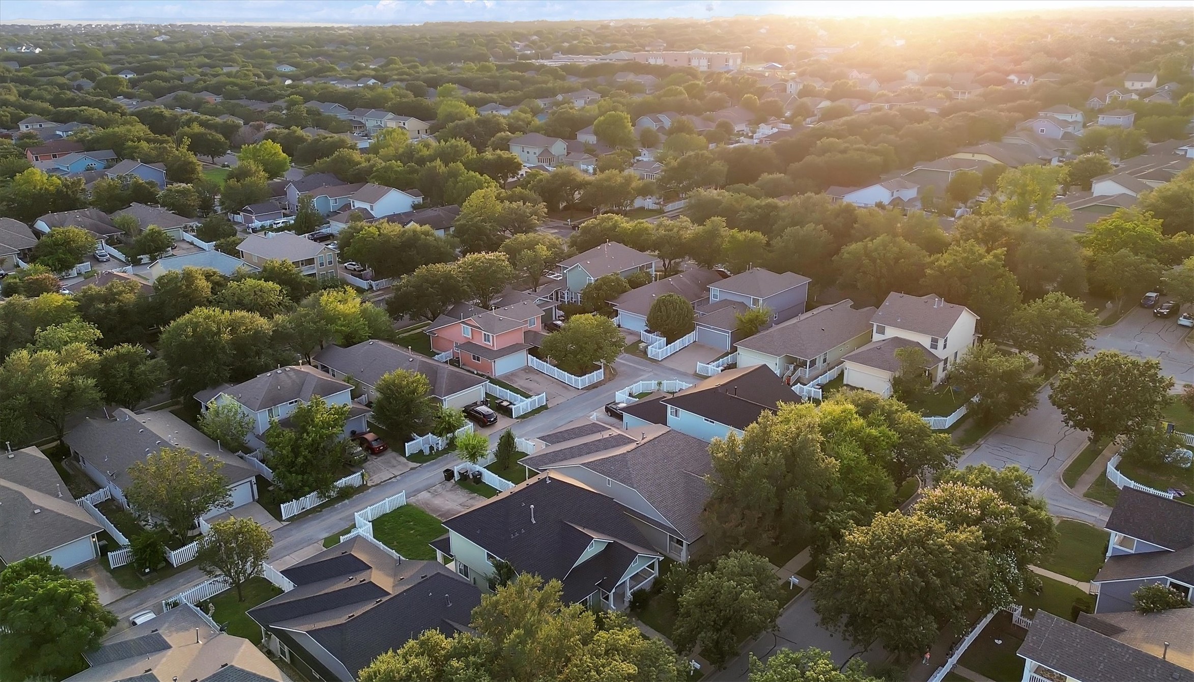 627 Scheel Road Kyle, TX 78640 - Photo 29 of 37 An aerial panorama reveals a residential area with many houses and lush greenery under a warm, glowing sky.