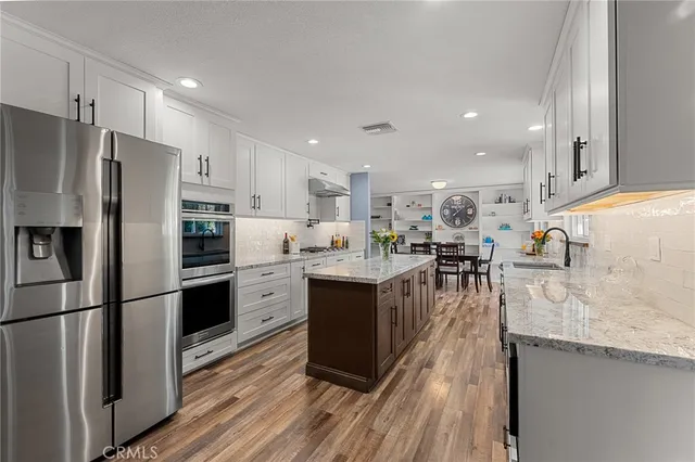 a kitchen with stainless steel appliances granite countertop a refrigerator a sink dishwasher a stove and a oven with wooden floor