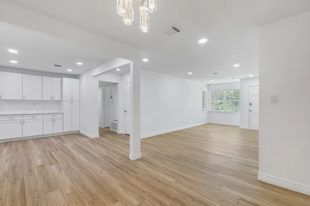 a view of an empty room with wooden floor kitchen and a window