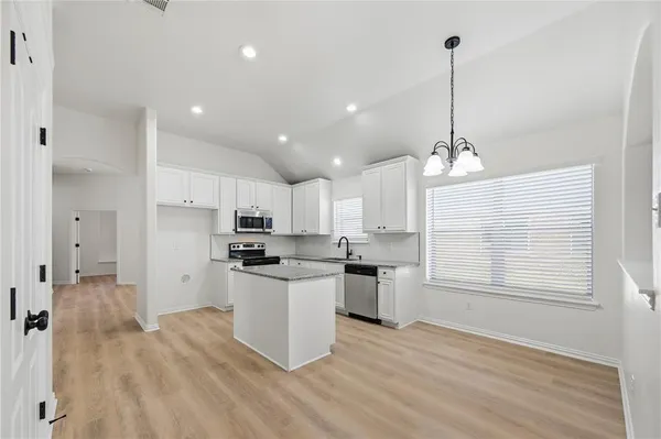 a kitchen with stainless steel appliances kitchen island granite countertop a sink a stove a refrigerator and white cabinets