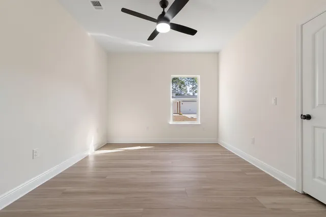 an empty room with wooden floor ceiling fan and windows