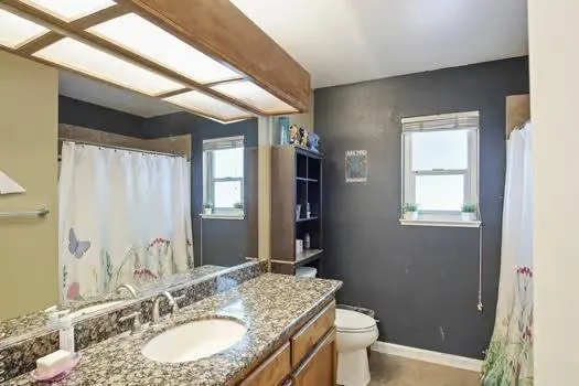 a bathroom with a granite countertop sink a toilet a mirror and shower
