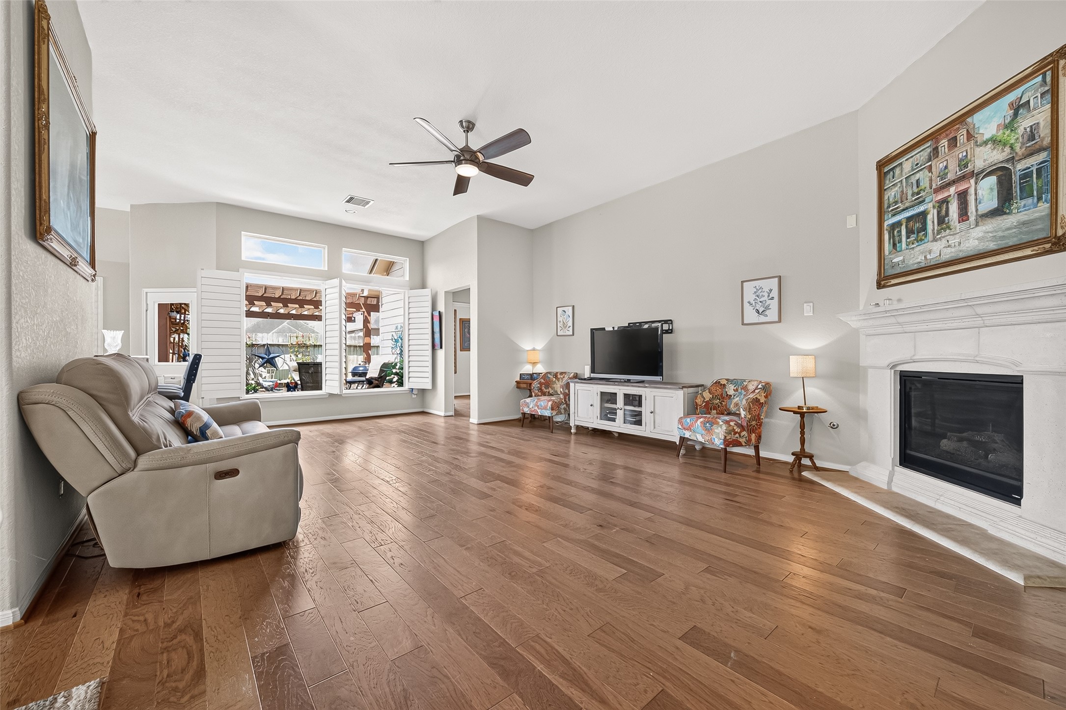 4910 Culver Lane Rosenberg, TX 77471 - Photo 3 of 50 This spacious living room features engineered wood floors, a cozy fireplace, and abundant natural light from large windows with shutters. The open layout is complemented by neutral walls and stylish ceiling fan, creating a welcoming atmosphere perfect for relaxation and entertainment.