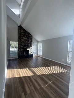 a view of an empty room with wooden floor fire place and windows