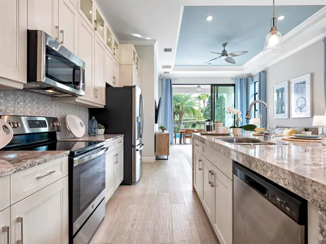 a kitchen with stainless steel appliances granite countertop a stove top oven a sink dishwasher a refrigerator and a dining table with wooden floor
