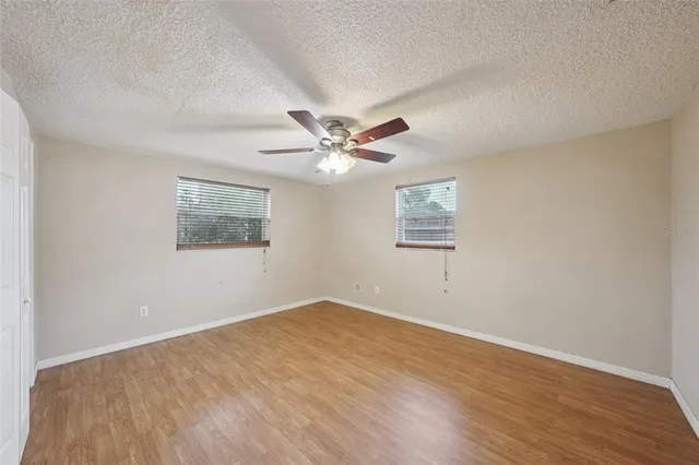 an empty room with wooden floor ceiling fan and windows