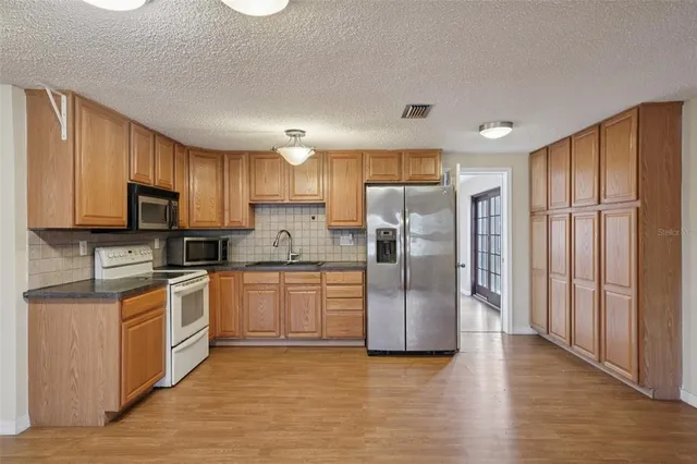 a kitchen with stainless steel appliances granite countertop a refrigerator a sink dishwasher a stove top oven a refrigerator and white cabinets with wooden floor