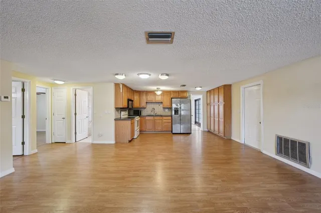 a view of an empty room with wooden floor and a kitchen