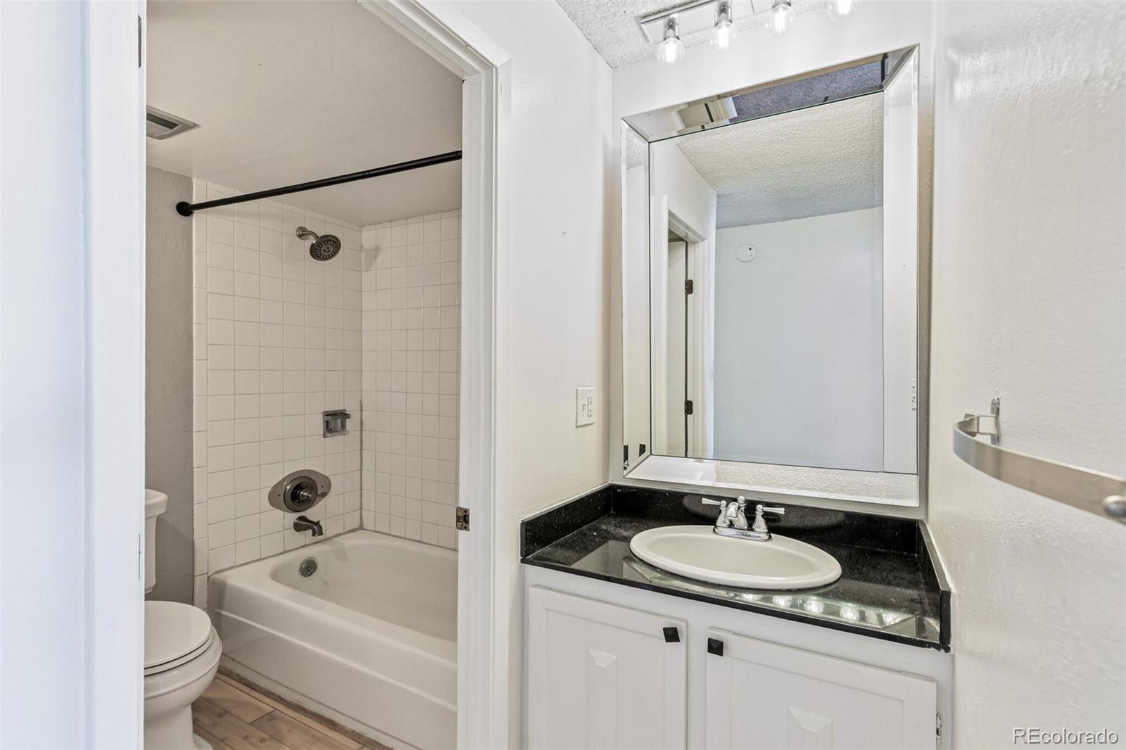 2 Adams Street, Unit 910 Denver, CO 80206 - Photo 10 of 15 a bathroom with a granite countertop sink a toilet a mirror and shower