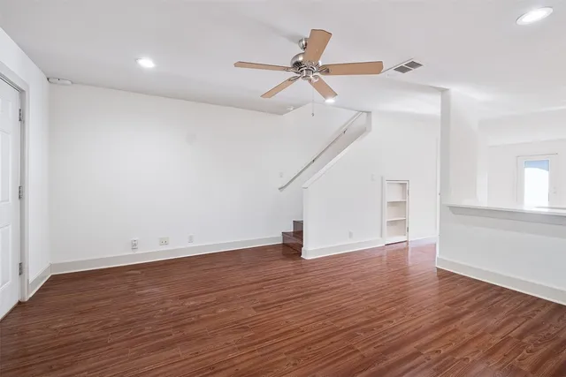 a view of an empty room with wooden floor and a ceiling fan