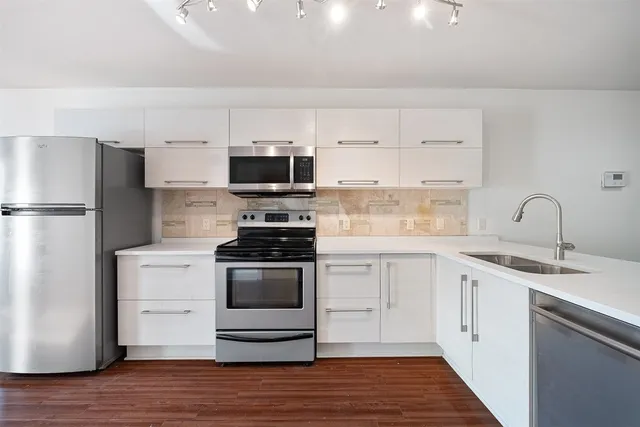 a kitchen with stainless steel appliances a sink cabinets and a wooden floor