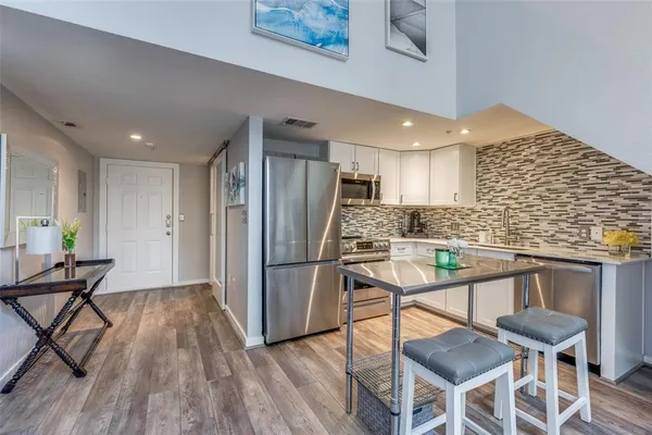 a kitchen with stainless steel appliances kitchen island granite countertop a dining table chairs and a refrigerator
