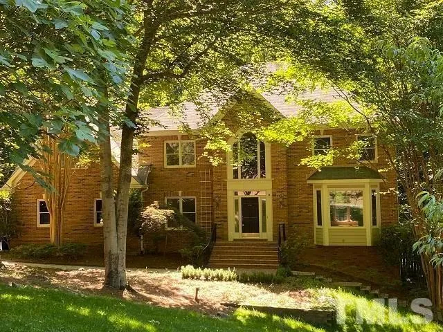 a view of a brick house next to a yard with large tree