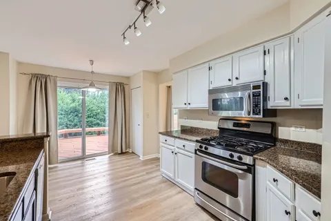 a kitchen with stainless steel appliances granite countertop a stove a sink and white cabinets with wooden floor