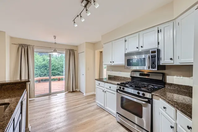 a kitchen with stainless steel appliances granite countertop a stove a sink and white cabinets with wooden floor