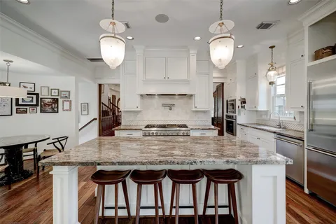 a kitchen with stainless steel appliances granite countertop a stove top oven a refrigerator a sink dishwasher a dining table and chairs with wooden floor