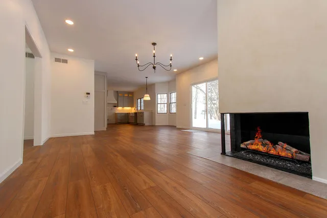 an empty room with wooden floor fire place and windows